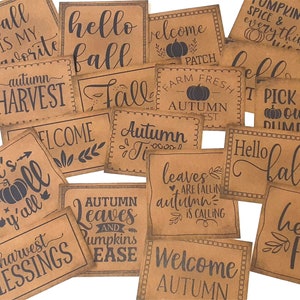 May include: A collection of 14 brown paper signs with black text, featuring various autumn-themed phrases like "fall is my favorite", "hello fall", "autumn harvest", "welcome autumn", "leaves are falling autumn is calling", and "pick your own pumpkins".