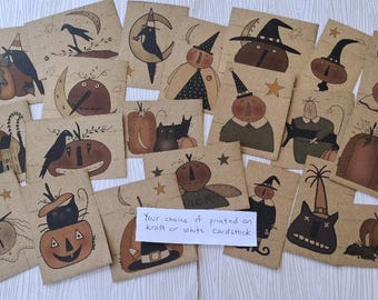 May include: A collection of rectangular kraft paper cards featuring various hand-drawn illustrations of pumpkins, black cats, crows, and witches in hats. A small white rectangular note in the center reads: Your choice of printed on kraft or white cardstock.