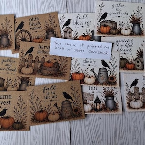 May include: A collection of rectangular cards featuring autumn-themed illustrations of pumpkins, crows, and rustic items like watering cans and lanterns. Each card displays seasonal text such as fall blessings, autumn harvest, and gather and give thanks.