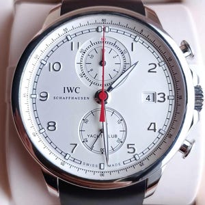 Peut inclure: Une montre chronographe IWC Schaffhausen avec un cadran blanc, des chiffres arabes noirs et un guichet de date à trois heures. Elle présente une aiguille de chronographe centrale rouge, deux sous-cadrans et un bracelet en caoutchouc noir texturé.