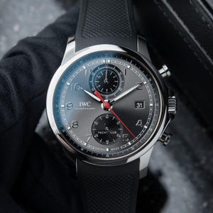 Peut inclure: Une montre chronographe IWC Schaffhausen Yacht Club en acier inoxydable avec un cadran gris soleillé, des sous-cadrans noirs, des chiffres arabes, un guichet de date à trois heures, une aiguille de chronographe rouge et un bracelet en caoutchouc noir.
