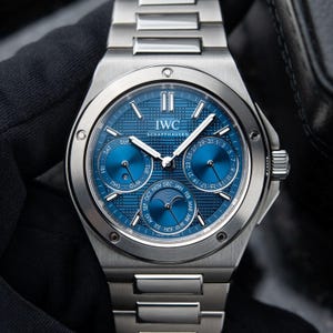 Peut inclure: Une montre-bracelet en acier inoxydable argenté dotée d'un cadran bleu avec un motif à grille texturé. La montre comprend trois sous-cadrans pour le jour, la date et le mois, un indicateur de phase de lune et le texte IWC SCHAFFHAUSEN.