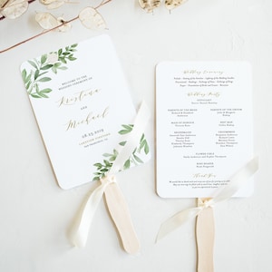 Peut inclure: Un éventail de programme de cérémonie de mariage avec un motif aquarelle de feuilles vertes et de fleurs blanches. L'éventail est en papier et possède une poignée en bois. Le programme comprend les noms de la mariée et du marié, la date du mariage et les noms des membres de la noce.