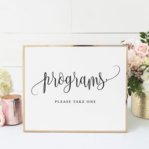 May include: A white sign with a gold frame that says "programs" in cursive script. Below the word "programs" it says "please take one".