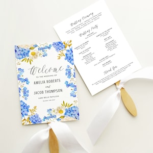 Può includere: Un ventaglio con programma di nozze con un design floreale con fiori blu e bianchi. Il ventaglio è decorato con un nastro bianco e un manico in legno. Il programma include i nomi degli sposi, Amelia Roberts e Jacob Thompson, e la data del matrimonio, 18 dicembre 2023. Il programma include anche i nomi dei membri del matrimonio e l'ordine degli eventi.