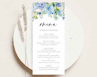 Op de afbeelding: Een aquarelmenukaart met blauwe en witte bloemen. De tekst luidt "Menu", "Stefanie & Nicolas", en somt de gangen op voor een huwelijksreceptie: "Eerste Gang", "Tweede Gang", "Hoofdgerecht" en "Dessert".