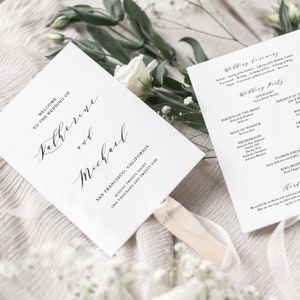 Könnte beinhalten: Ein weißer Hochzeitsprogramm-Fächer mit schwarzem Kalligraphie-Text. Der Text lautet "Willkommen zur Hochzeit von Katherine und Michael, San Francisco, Kalifornien, achtundzwanzigster August zweitausend einundzwanzig".