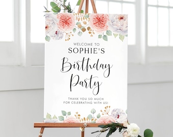 May include: A white welcome sign with pink and white flowers and gold accents. The sign reads "Welcome to Sophie's Birthday Party. Thank you so much for celebrating with us!"