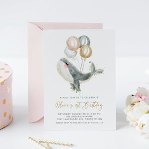 May include: A light blue whale with gold glitter and pink cheeks is holding onto a bunch of balloons in shades of pink, gray, and gold. The text "Oliver's 1st Birthday" is written in gold script. The invitation also includes the date, time, location, and RSVP information.