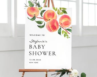 May include: A white rectangular welcome sign for a baby shower featuring a watercolour illustration of peaches on branches with green leaves. The text reads: WELCOME TO Stefanie's BABY SHOWER 12.08.2045 NEW YORK. The sign is displayed on a wooden easel.