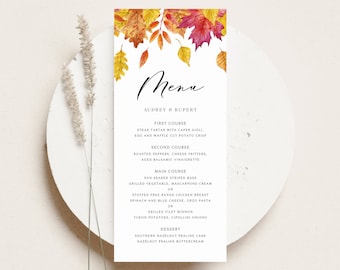 May include: A fall-themed wedding menu with watercolor illustrations of autumn leaves in shades of red, orange, and yellow. The menu lists the courses: First Course, Second Course, Main Course, and Dessert. The text reads: "Menu, Audrey & Rupert, First Course, Steak Tartar with Caper Aioli, Egg and Waffle Cut Potato Crisp, Second Course, Roasted Peppers, Cheese Fritters, Aged Balsamic Vinaigrette, Main Course, Pan Seared Striped Bass, Grilled Vegetable, Mascarpone Cream or Stuffed Free Range Chicken Breast, Spinach and Blue Cheese, Orzo Pasta or Grilled Filet Mignon, Yukon Potatoes, Cipollini Onions, Dessert, Southern Hazelnut Praline Cake, Hazelnut Praline Buttercream, Belle Hanah Paperie."