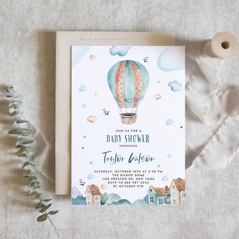 This printable baby shower invitation features a whimsical watercolor design with a pastel hot air balloon floating above a charming village scene. The background includes tiny houses, trees, and rolling hills. Editable shower details are centered in soft script and serif fonts, perfect for a dreamy, storybook-themed baby shower.
