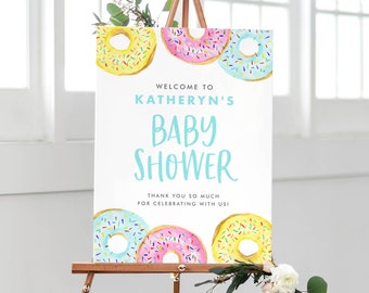 Puede incluir: Bienvenido al Baby Shower de Katheryn con temática de donas. El cartel presenta tres donas con coloridos espolvoreados sobre un fondo blanco.