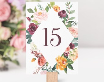May include: A white card with a floral design in shades of pink, orange, and burgundy. The card has a diamond-shaped frame with the number 15 in the center. The card is on a wooden stand.