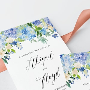 May include: Wedding programme featuring a watercolour design of blue and white hydrangeas and white roses. The text reads "Welcome to the wedding of Abigail and Floyd".