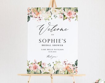May include: A white welcome sign with floral borders in shades of pink, peach, and green. The text reads "Welcome to Sophie's Bridal Shower, Lake Belle Pavilion, 12.08.2045, thank you!"