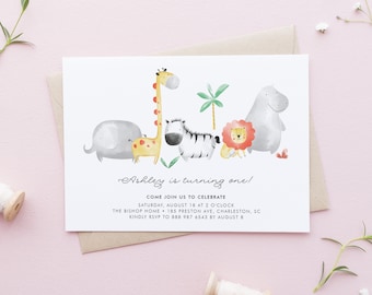 May include: A white invitation card with a watercolor illustration of a giraffe, zebra, elephant, lion, and hippopotamus. The text on the card reads "Ashley is turning one!" and includes details about the birthday party, including the date, time, location, and RSVP information.