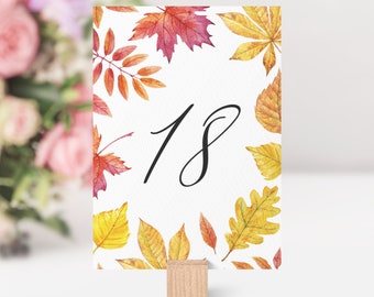 May include: A white card with a watercolor design of fall leaves in shades of red, orange, and yellow. The number 18 is written in black cursive script on the card.