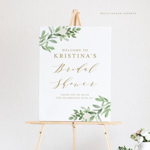 May include: White sign with green watercolor floral border and gold lettering. The sign reads "Welcome to Kristina's Bridal Shower. Thank you so much for celebrating with us!"