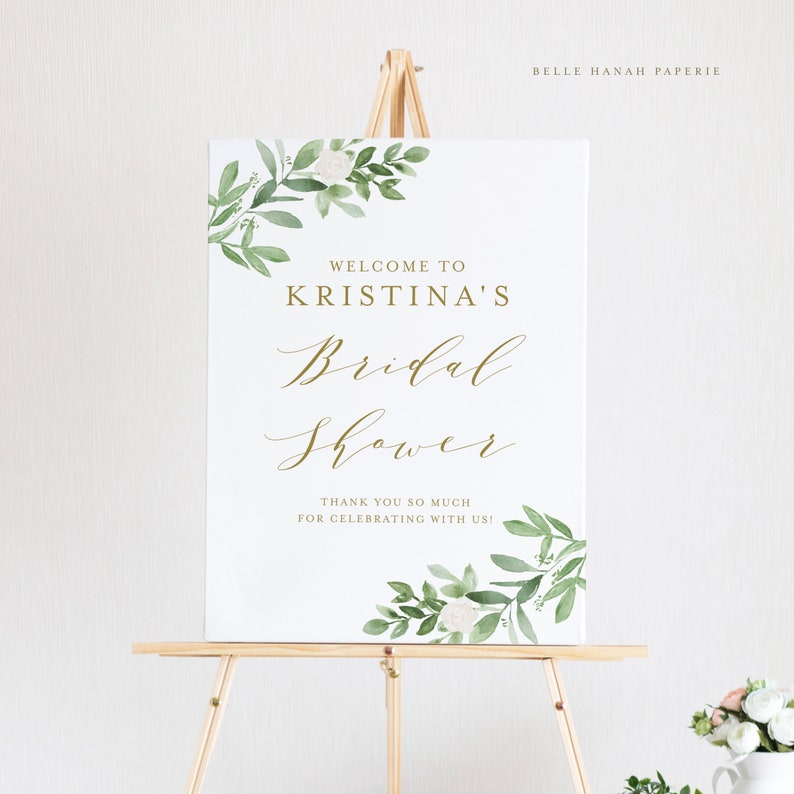 May include: White sign with green watercolor floral border and gold lettering. The sign reads "Welcome to Kristina's Bridal Shower. Thank you so much for celebrating with us!"