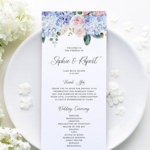 Op de afbeelding: Een programma voor een huwelijksceremonie met een aquarelbloemendesign met blauwe en roze bloemen. Het programma geeft de volgorde van de gebeurtenissen voor de bruiloft van Sophie en Rupert weer, die plaatsvindt op 15 december 2025 in Lake Belle Manor.