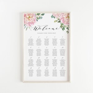 May include: A white framed seating chart with a floral design featuring pink peonies and greenery. The chart is titled "Welcome" and includes a list of names for each table number.