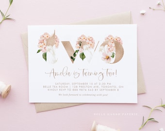 May include: A white invitation card with gold lettering that says "Anelia is turning Two!" The card is decorated with pink and white flowers. The text below the main text says "Saturday, September 15 at 2:30 PM Belle Tea Room | 128 Preston Ave, Toronto, ON Kindly RSVP to 888 9876 543 by September 8 We look forward to celebrating with you! Belle Hanah Paperie"