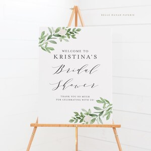 May include: White sign with green foliage and white flowers. The sign says "Welcome to Kristina's Bridal Shower. Thank you so much for celebrating with us!"  Belle Hanah Paperie.
