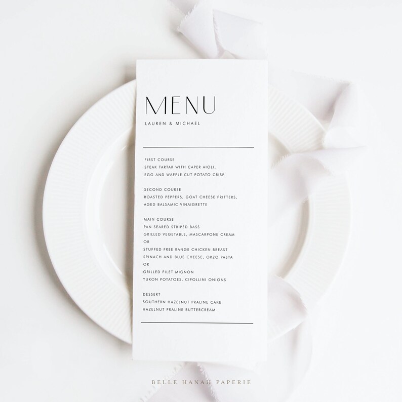 May include: A minimalist wedding menu card with a black and white design. The menu features a variety of dishes, including steak tartar, roasted peppers, pan seared striped bass, and hazelnut praline cake. The card is printed on high-quality paper and features a simple, elegant design.