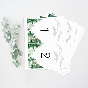 Op de afbeelding: Een set bedrukbare tafelkaartjes met een aquarel bosontwerp. De nummers 1 en 2 zijn in zwart op de kaartjes gedrukt.