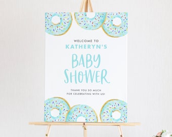 Puede incluir: Un letrero de bienvenida para baby shower sobre un caballete de madera. El letrero presenta un fondo azul claro con donas de acuarela y el texto "Welcome to Kathryn's Baby Shower". El letrero también incluye el texto "Thank you so much for celebrating with us!"