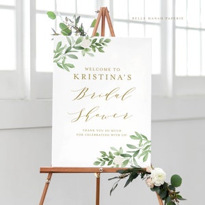 May include: White sign with green foliage and white flowers around the border. The text on the sign reads "Welcome to Kristina's Bridal Shower. Thank you so much for celebrating with us!"