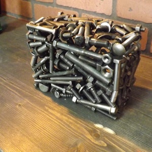 May include: A cube-shaped sculpture made entirely of metal bolts and nuts. The sculpture is made of a variety of sizes and shapes of bolts and nuts, all of which are arranged in a random pattern. The sculpture is a unique and interesting piece of art.