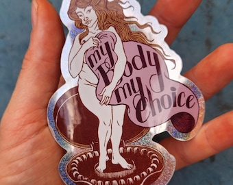 Puede incluir: Una pegatina holográfica con una ilustración de líneas de una figura de pie en una concha, sosteniendo una tela de color púrpura claro con el texto "my body my choice" escrito en letra cursiva de color púrpura oscuro. Acabado brillante.