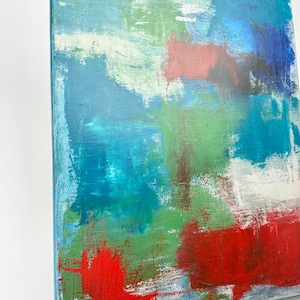 May include: An abstract painting on canvas featuring layered brushstrokes in vibrant shades of red, bright green, turquoise, and deep blue. The composition includes patches of white and textured paint application, with a signature visible in the bottom corner.