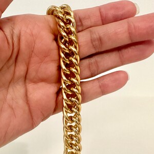 May include: A gold-toned metal chain bracelet featuring thick, interlocking oval links. The bracelet has a polished, reflective surface and a substantial, heavy-duty design. It is a classic piece of jewelry with a uniform link pattern throughout.