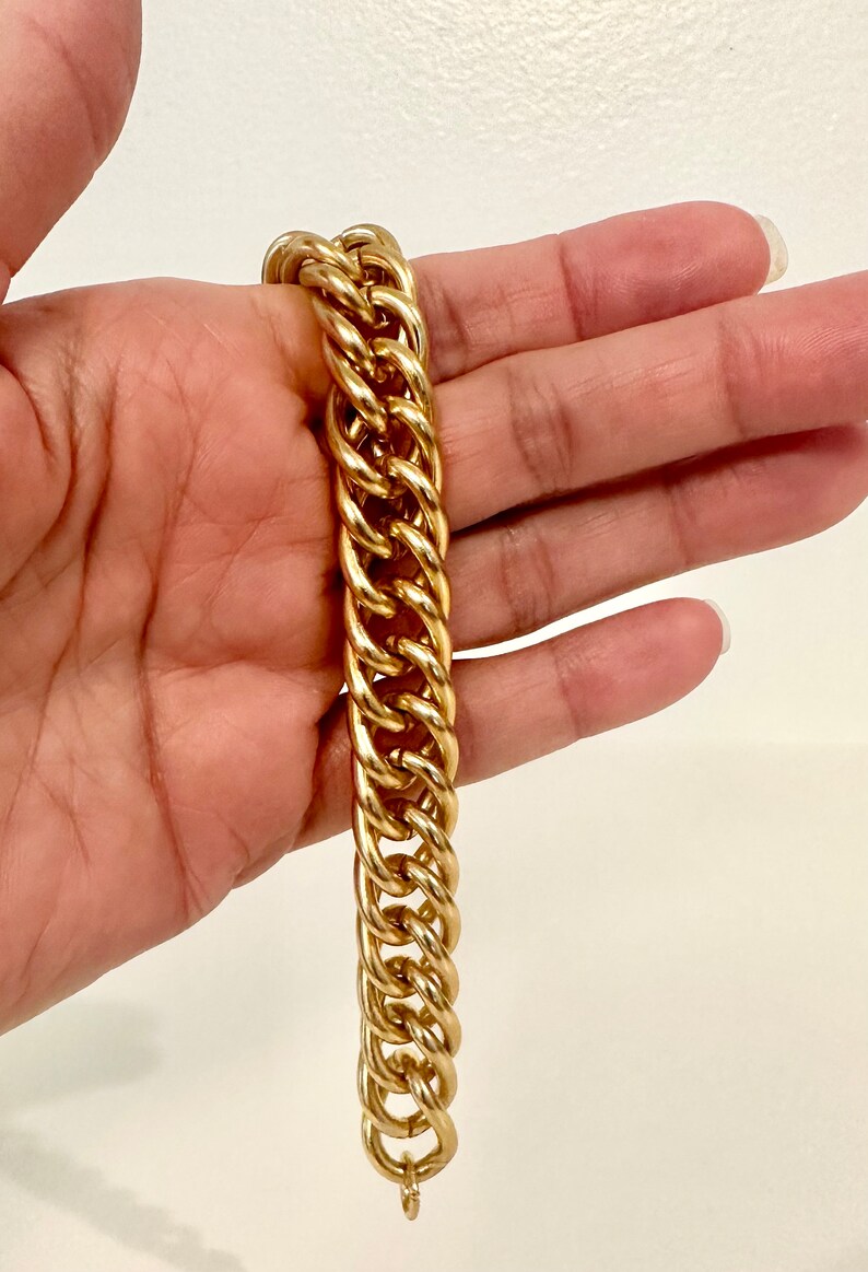May include: A gold-toned metal chain bracelet featuring thick, interlocking oval links. The bracelet has a polished, reflective surface and a substantial, heavy-duty design. It is a classic piece of jewelry with a uniform link pattern throughout.