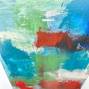 May include: An abstract painting on canvas featuring layered brushstrokes in shades of bright blue, teal, and light green, contrasted by bold, horizontal patches of deep red and dark brown, with visible texture from the paint application on the surface.
