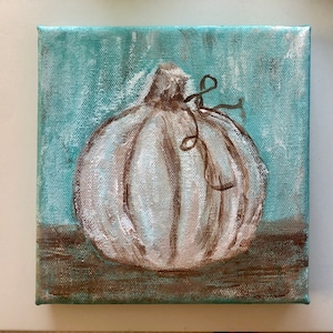 May include: A square canvas painting featuring a white pumpkin with brown brushstroke details and a small brown vine accent. The pumpkin is set against a textured light blue background with a brown horizontal band at the bottom of the composition.