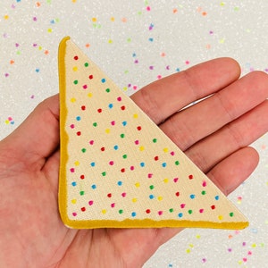 May include: A triangular shaped patch with a white background and a yellow border. The patch is covered in colourful sprinkles.