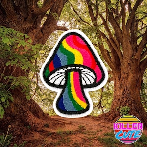May include: Rainbow embroidered patch of a mushroom with a white stem and a rainbow cap. The patch is on a white background and is surrounded by green trees.