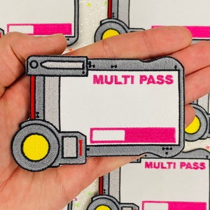 May include: An embroidered patch in grey and red with a white background. The patch features a stylised image of a device with a yellow circle and the text "MULTI PASS".