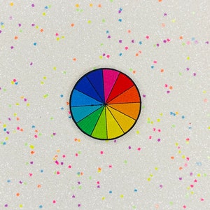 May include: A colorful rainbow color wheel patch with a black outline. The patch is on a white background with small, colorful glitter stars.