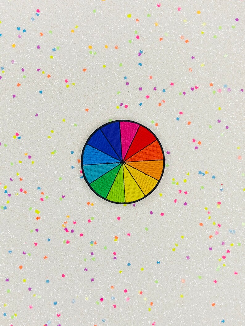 May include: A colorful rainbow color wheel patch with a black outline. The patch is on a white background with small, colorful glitter stars.