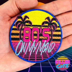 May include: A round, embroidered patch with a pink and blue 80's on my mind design. The patch features a yellow sun, palm trees, and a retro grid pattern.