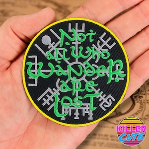 May include: A black and green embroidered patch with a compass design and the text "Not all who wander are lost".