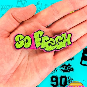 Pode incluir: Um remendo de ferro com o texto "So Fresh" em uma fonte de estilo graffiti, com letras verdes e rosas.