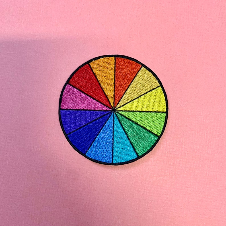 May include: A colorful embroidered patch in the shape of a circle, divided into 12 sections, each a different color of the rainbow.