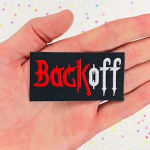 May include: Black iron-on patch with red and white embroidery that reads "Back Off" in a gothic font.
