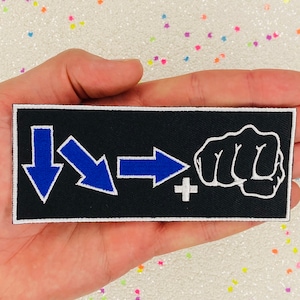 May include: Black embroidered patch with blue arrows pointing in different directions and a white plus sign. A white fist is on the right side of the patch.